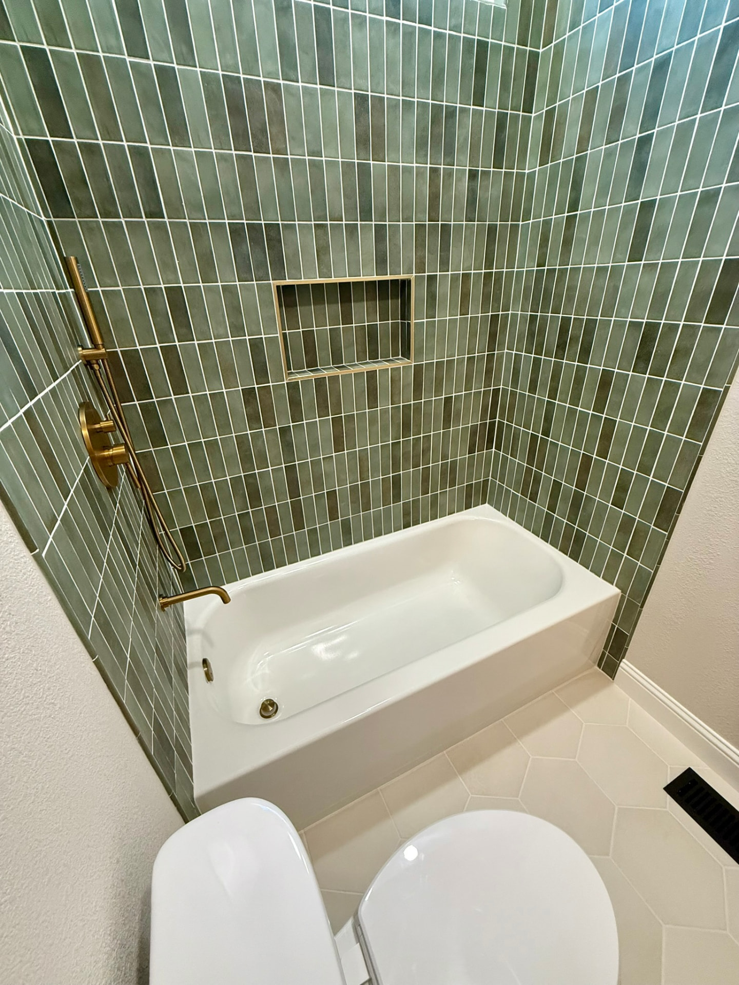 Tub with green vertical stacked tile and brass shower fixtures